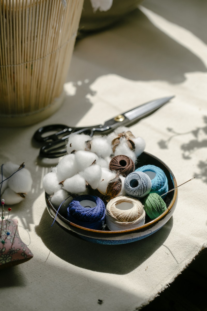 Thread bobbins with scissors and needles placed on table in atelier